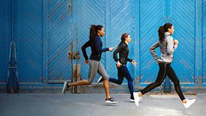 Three people jogging outdoors with a blue fenced background
