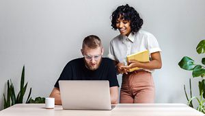Two people looking down at a laptop with plants either side of them in a room