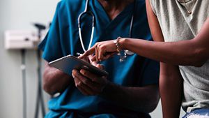 Person pointing at a mobile phone that a nurse is holding