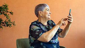 A person seaated taking a picture on her mobile with an orange wall background