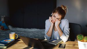 A young person leaning into her hands looking down at her laptop in their office