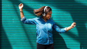 A person dancing listening to music with their headphones on with a green background outdoors