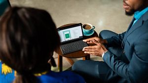Two people having a conversation with a laptop screen and a cup of coffee