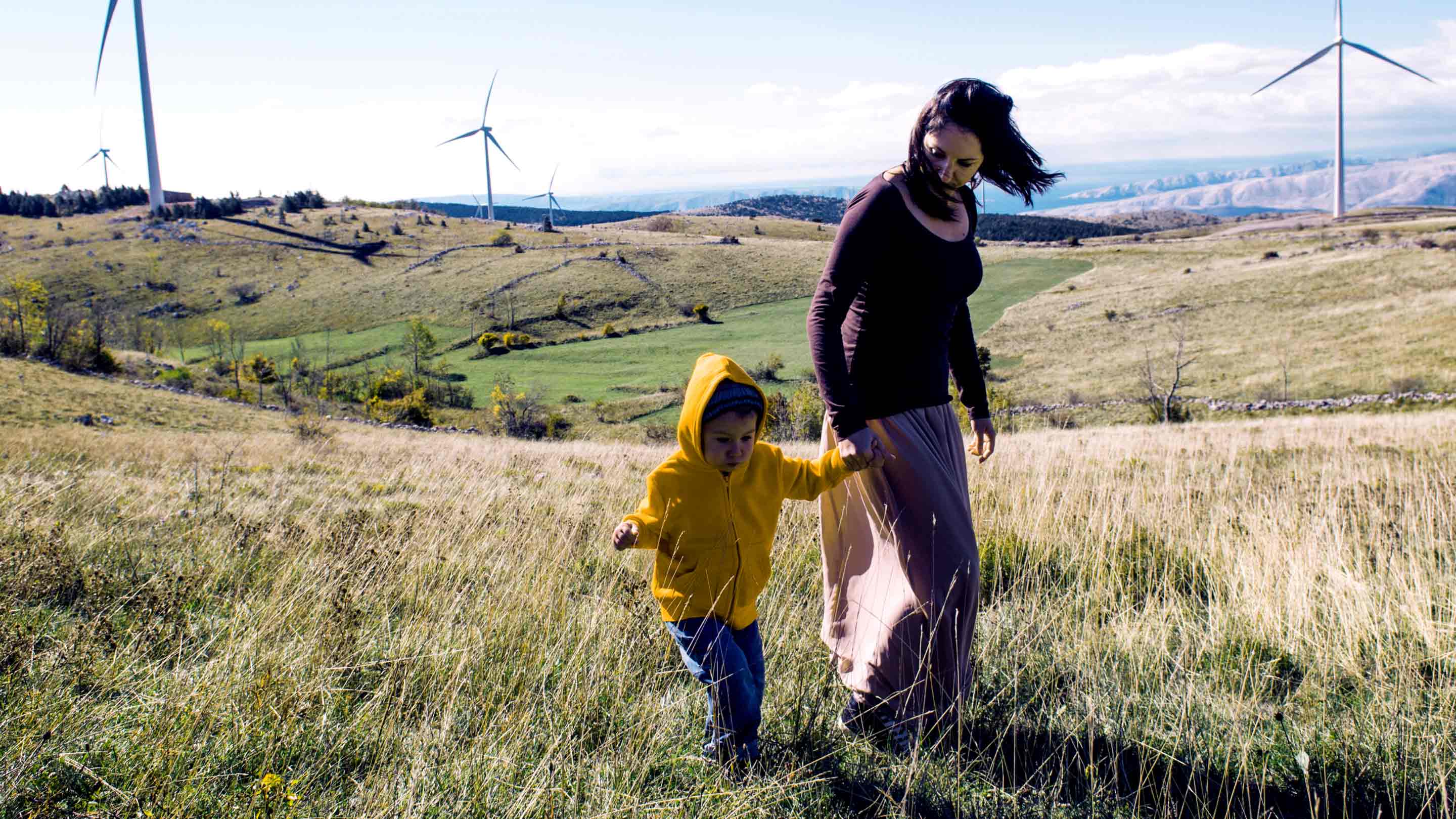 Woman and child walking across field; windy day, with windmills in the background