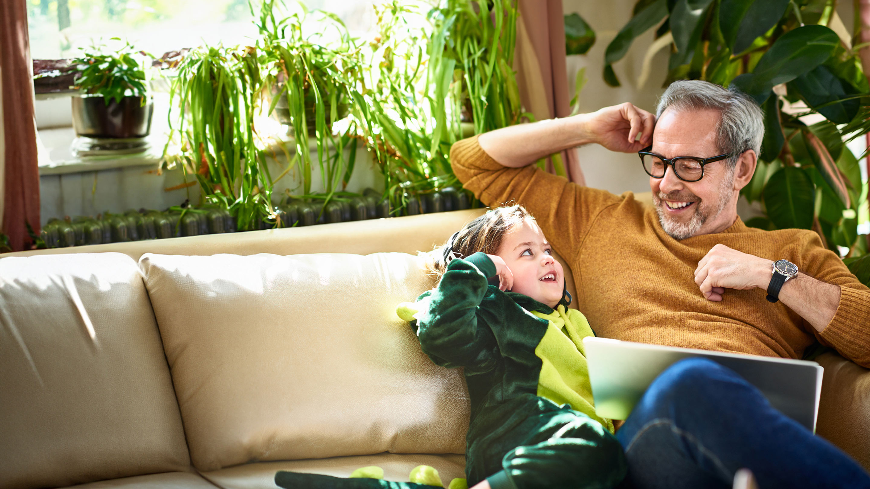 Adult with child dressed as a dinosaur sitting on a sofa together smiling