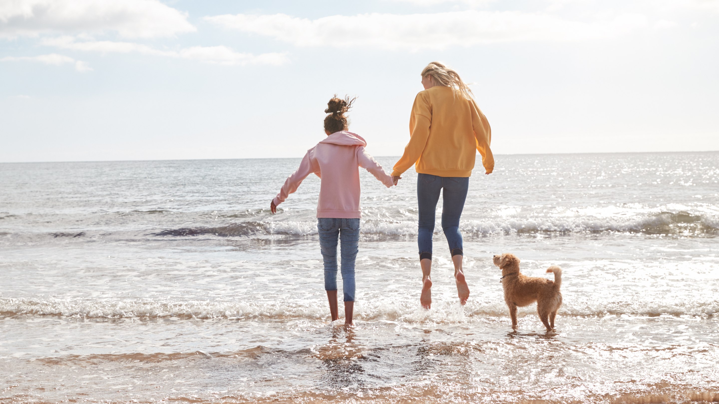 Mother and daughter playing with pet dog in waves on beach holiday