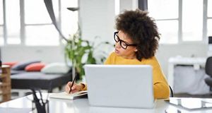 Woman sitting at a laptop making notes