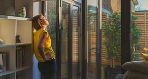 Woman standing in the sun looking out of bi fold windows