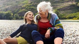 A grandparent sat with their grandchild, laughing on a beach, in an outdoor seaside setting