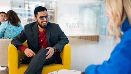 Man and women of different ages and ethnicities in joyful conversation sat on comfortable chairs in an office