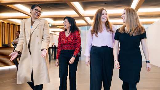 Four happy female business professionals walking together confidently into an office