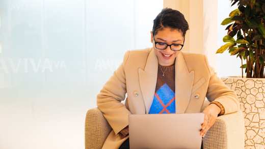 Women sat smiling looking at her laptop in a comfortable chair in her office