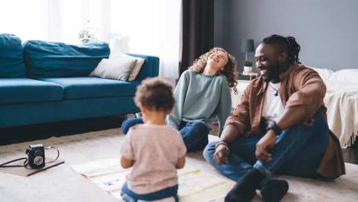 Two parents laughing together whilst playing with their child in their home
