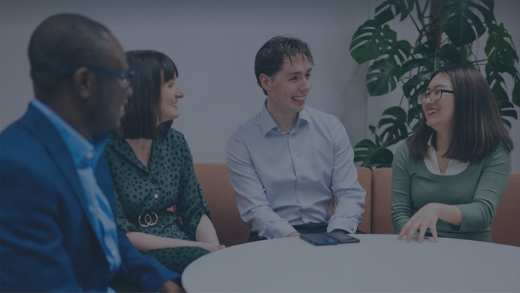 4 business professionals of various ages, genders and ethnicities sat around a table talking
