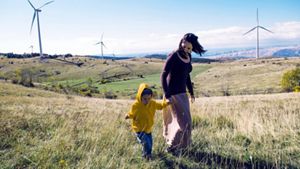 Person with their child walking through green landscape, with greener energy generating wind turbines in the background.