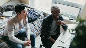 Male students looking at a computer in a bedroom