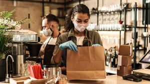 Two baristas serving coffee with masks and gloves on