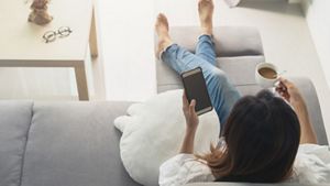 Woman relaxing on sofa with phone and a cup of tea