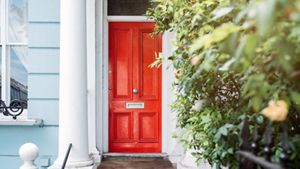 A red door to a home next to bushes
