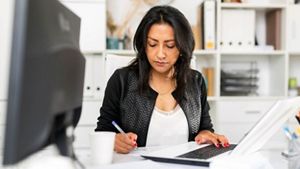 Person with their laptop and writing notes