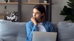 Person seated with hand on chin looking away from laptop