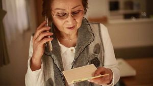 Person on the phone, reviewing a letter or message, in a home setting