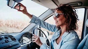 Person sat in the driving seat of their car, adjusting their rear view mirror