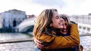 Two people smiling and hugging, with a cityscape in the background