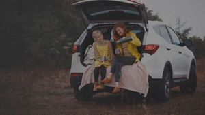 A mother pouring a hot drink for hyself and her daughter, sitting in the open boot of a car, in countryside setting.
