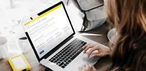 Person sat down using their laptop/MacBook looking at their investments portfolio, in a home setting