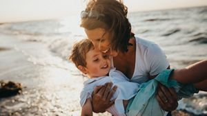 Mid-40s monther carrying her son on a beach, having fun