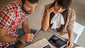 Two people sat at a table reviewing a laptop