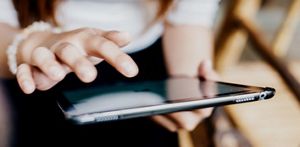 Close crop of a person sat down using their tablet device, in a home setting
