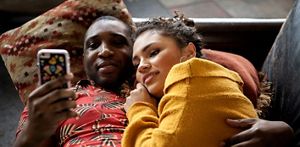 Couple looking at a phone while relaxing and cuddling on a sofa, in a home setting