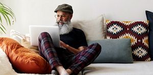 Person sitting up on a sofa against some cushions, using their laptop, in a home setting