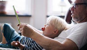 Person and a child sitting on a sofa, looking at a tablet device together, in a home setting