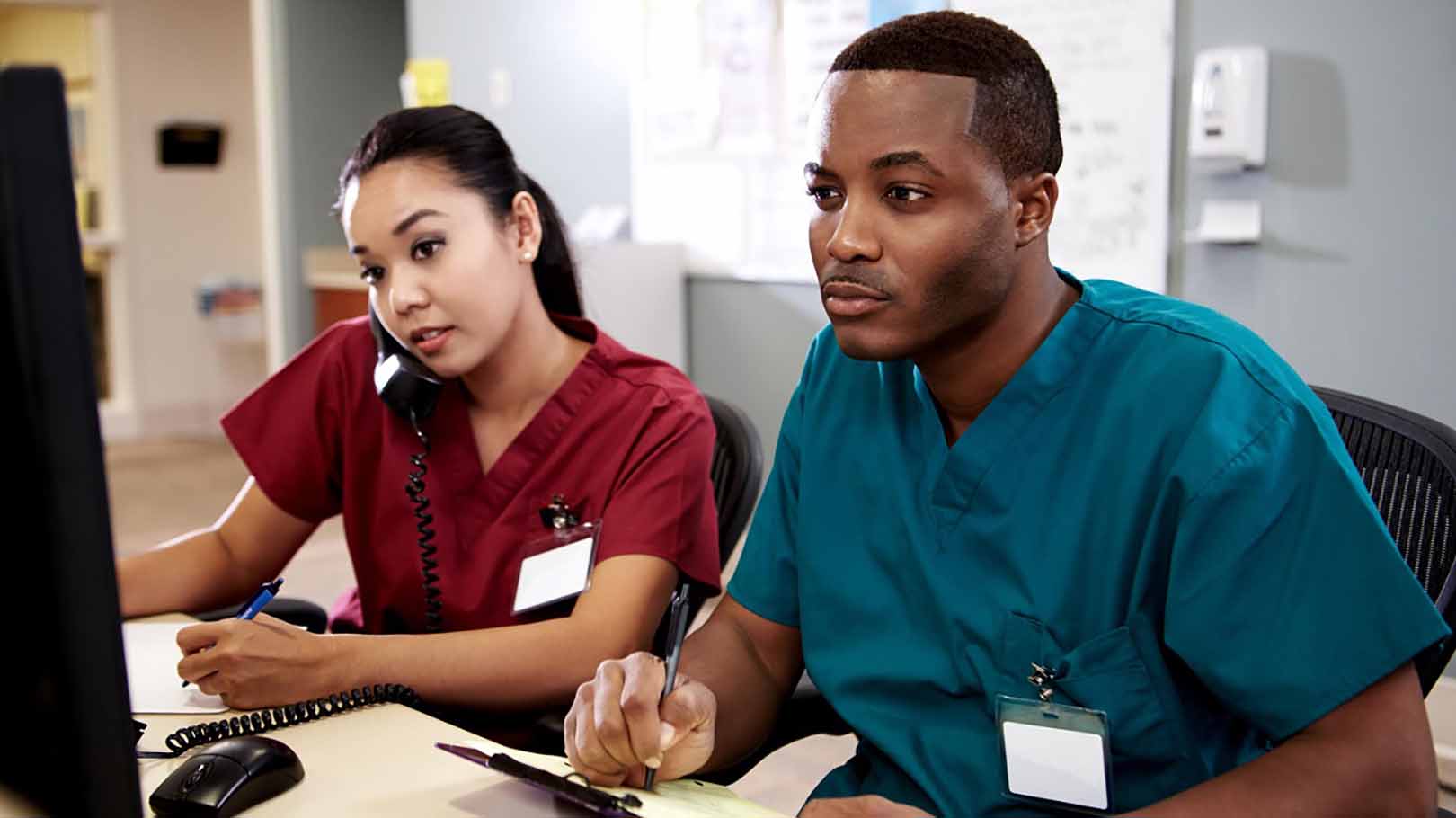 Medical experts making notes whilst reviewing a TV monitor and using the telephone