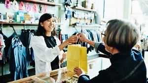 A picture of a woman handing a bag to a customer in a shop