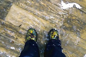 Feet close-up, waterproof boots, standing in a flood home with wooden floor