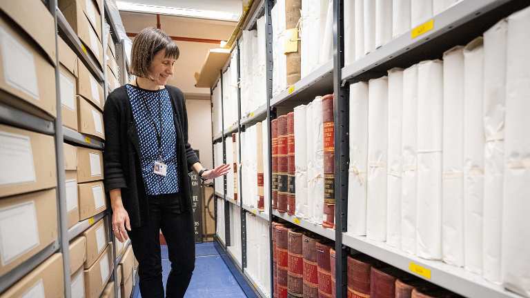Anna Stone in the archives, looking at a selection of large leatherbound books.