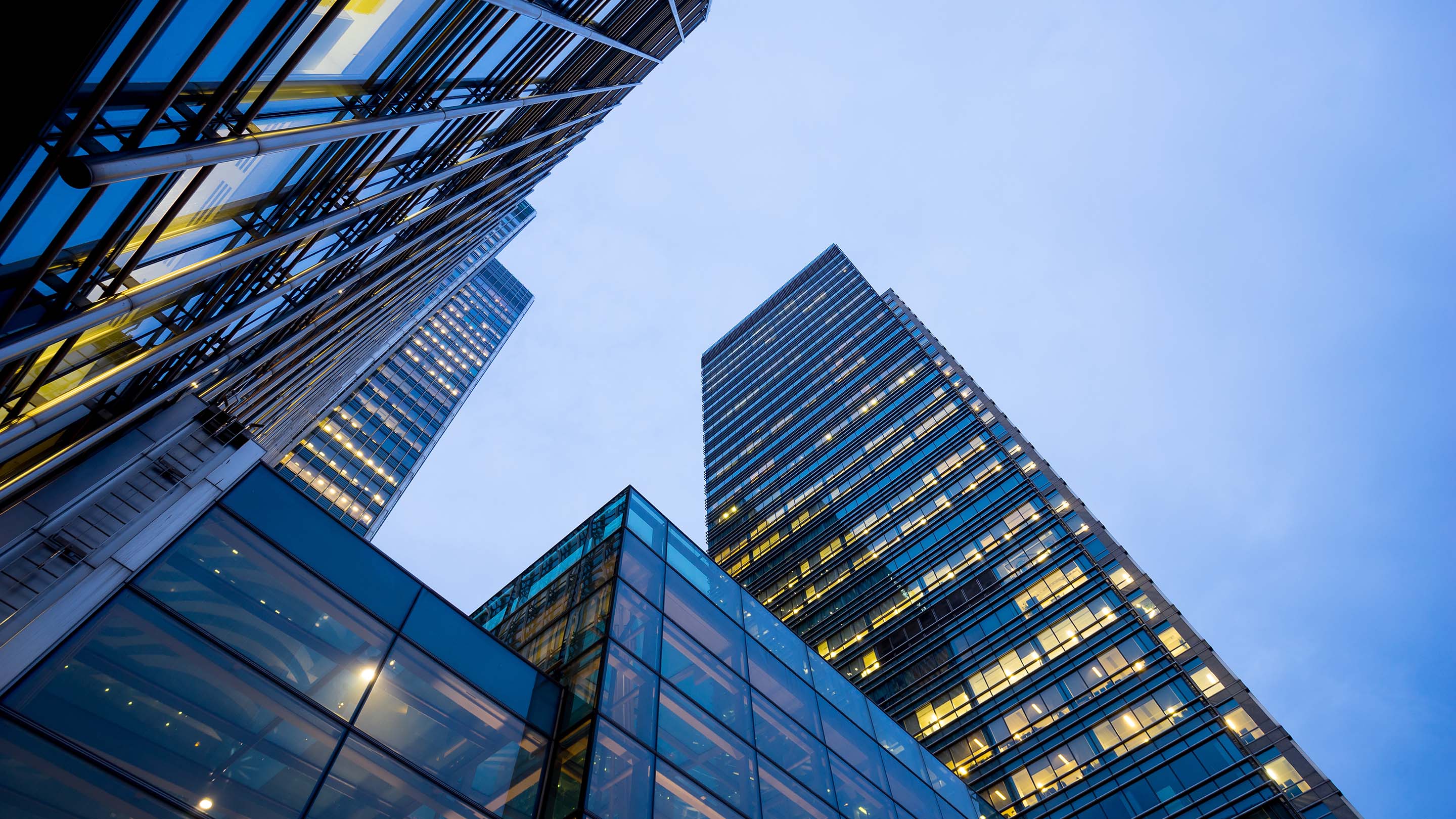 Modern skyscrapers at dawn/twilight, photograph taken from below looking up at them, lights shine from within the buildings