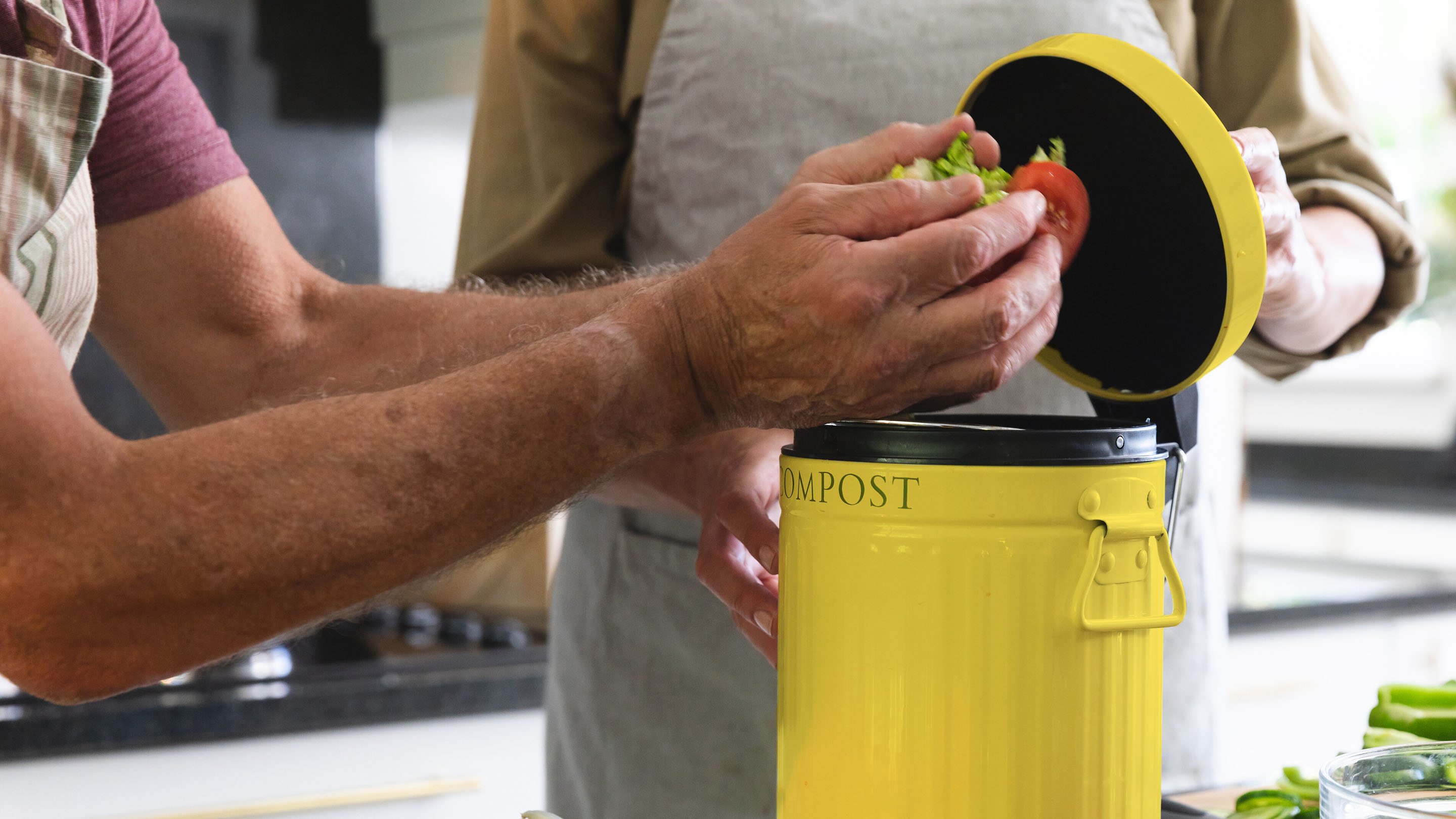 Person placing food waste into a yellow compost bin in a kitchen