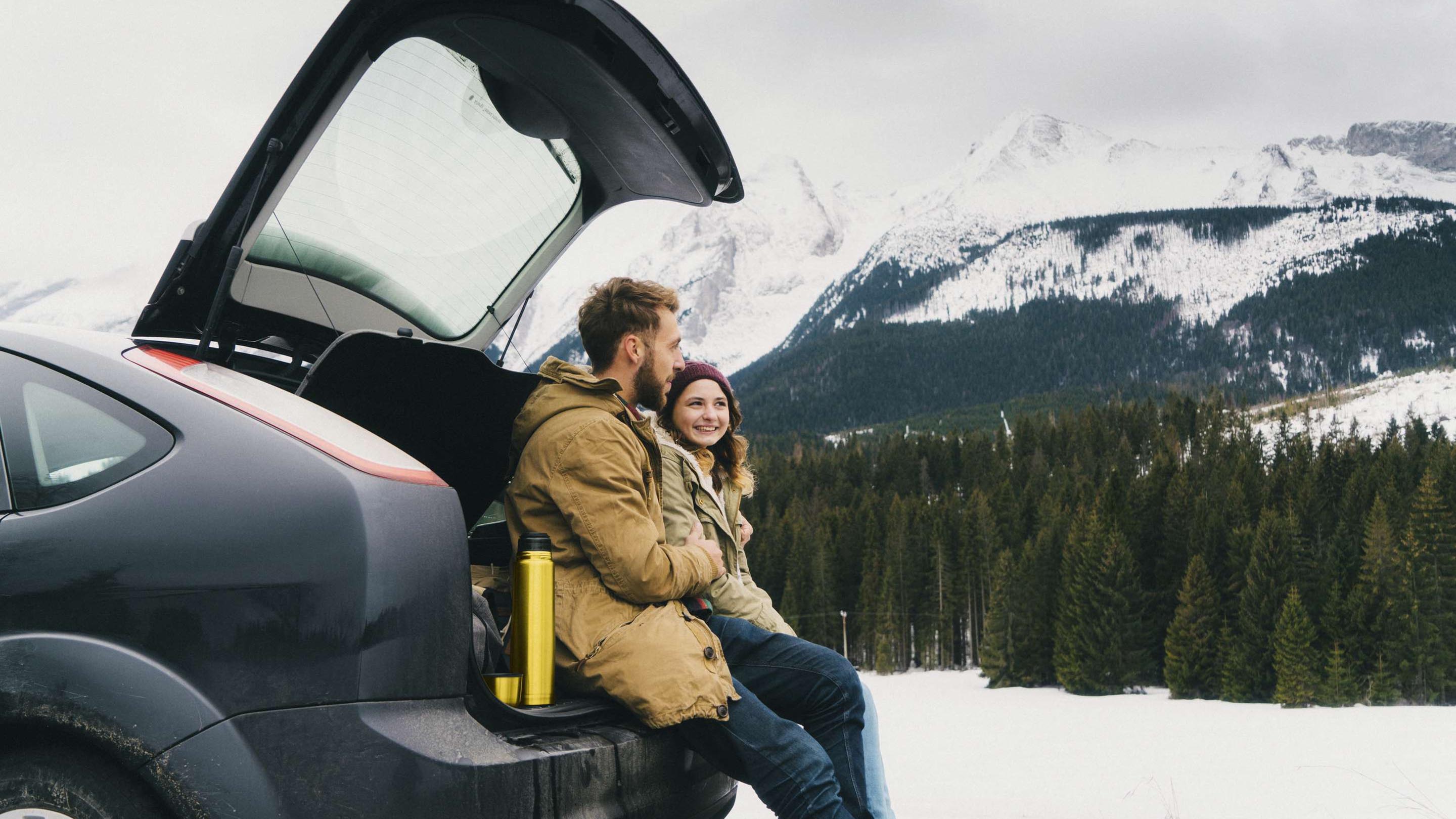 Man and woman sitting in car boot on snowy mountain