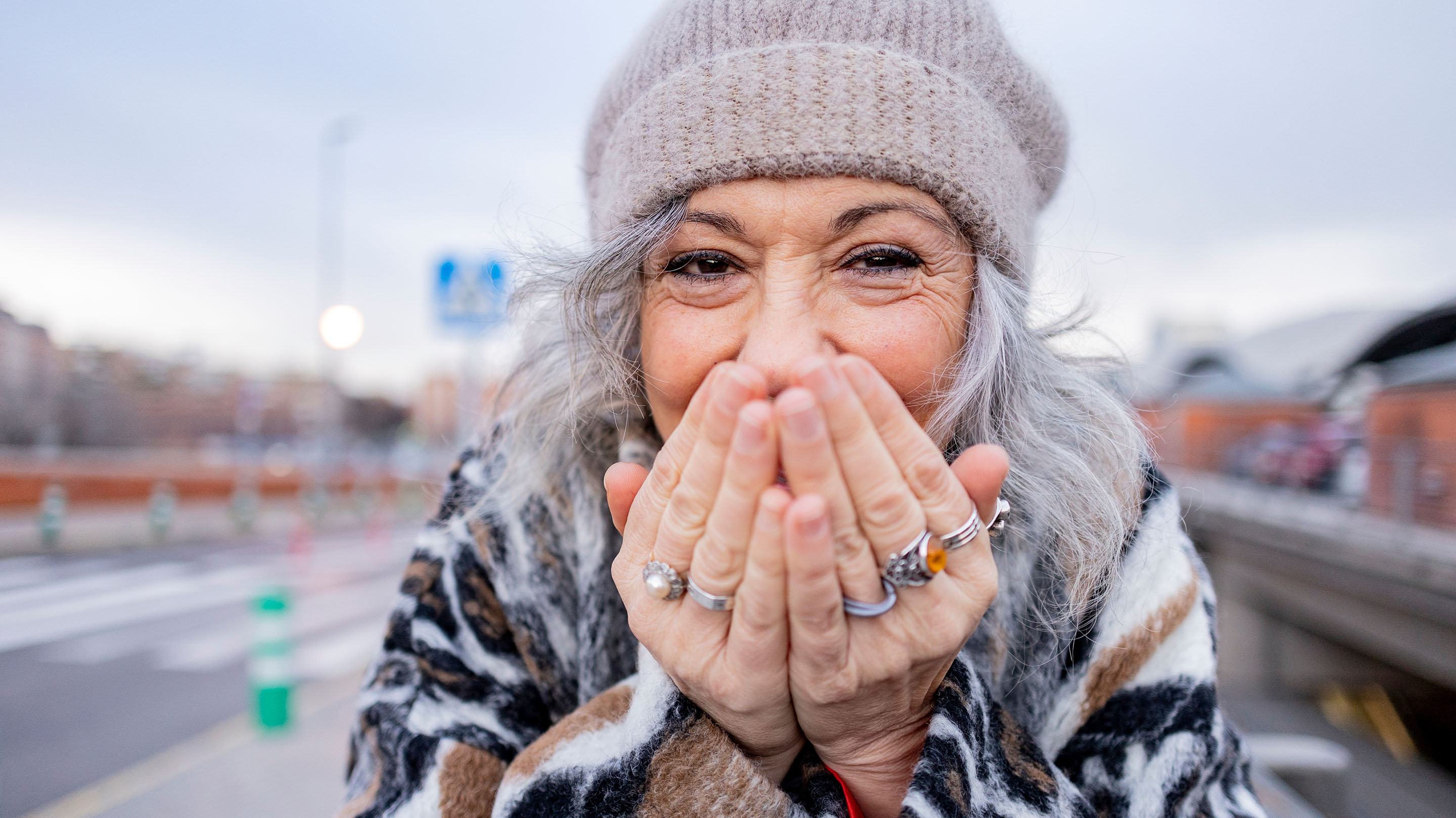 Person laughing and covering their mouth with their hands. They have several rings on their fingers.