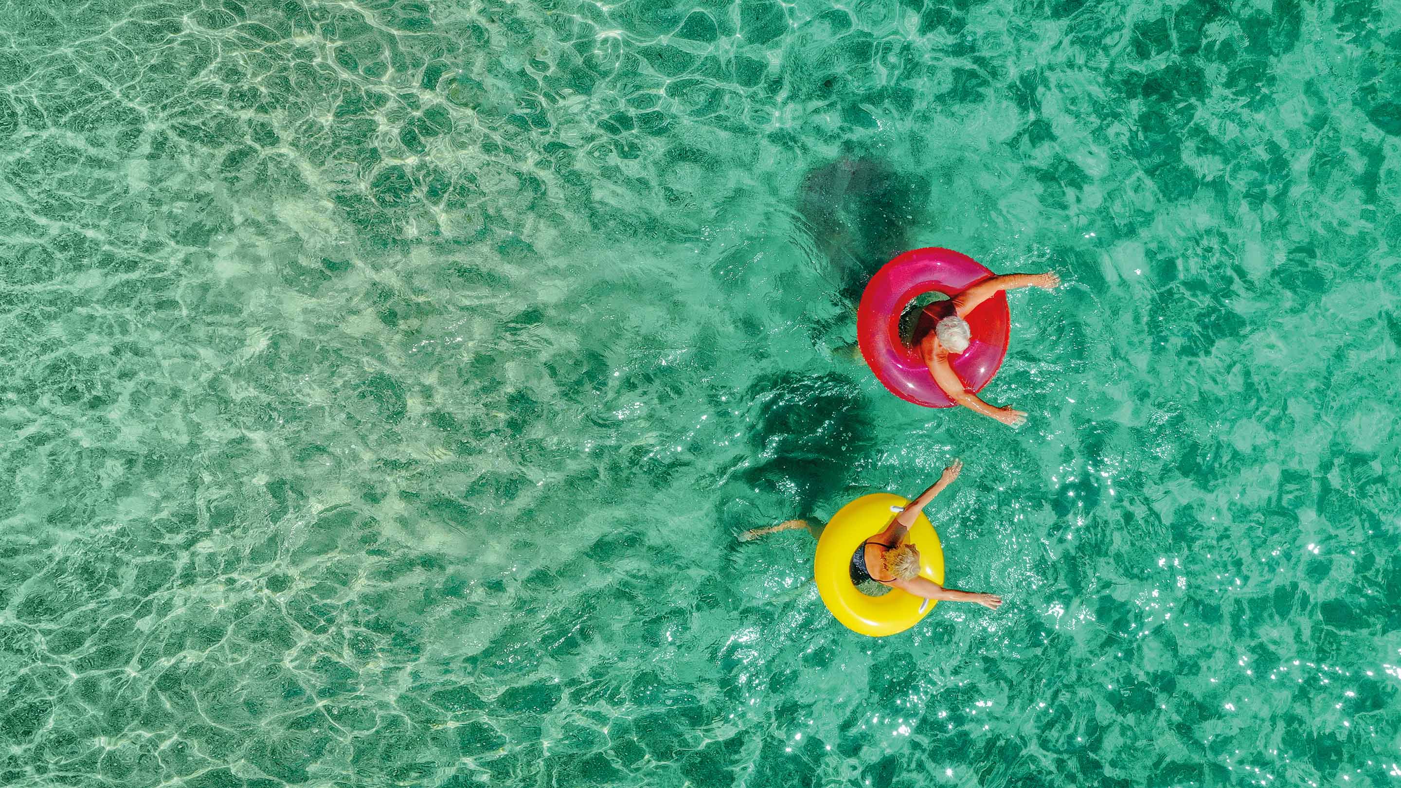 Overhead photo of two people floating in the ocean using colourful rings