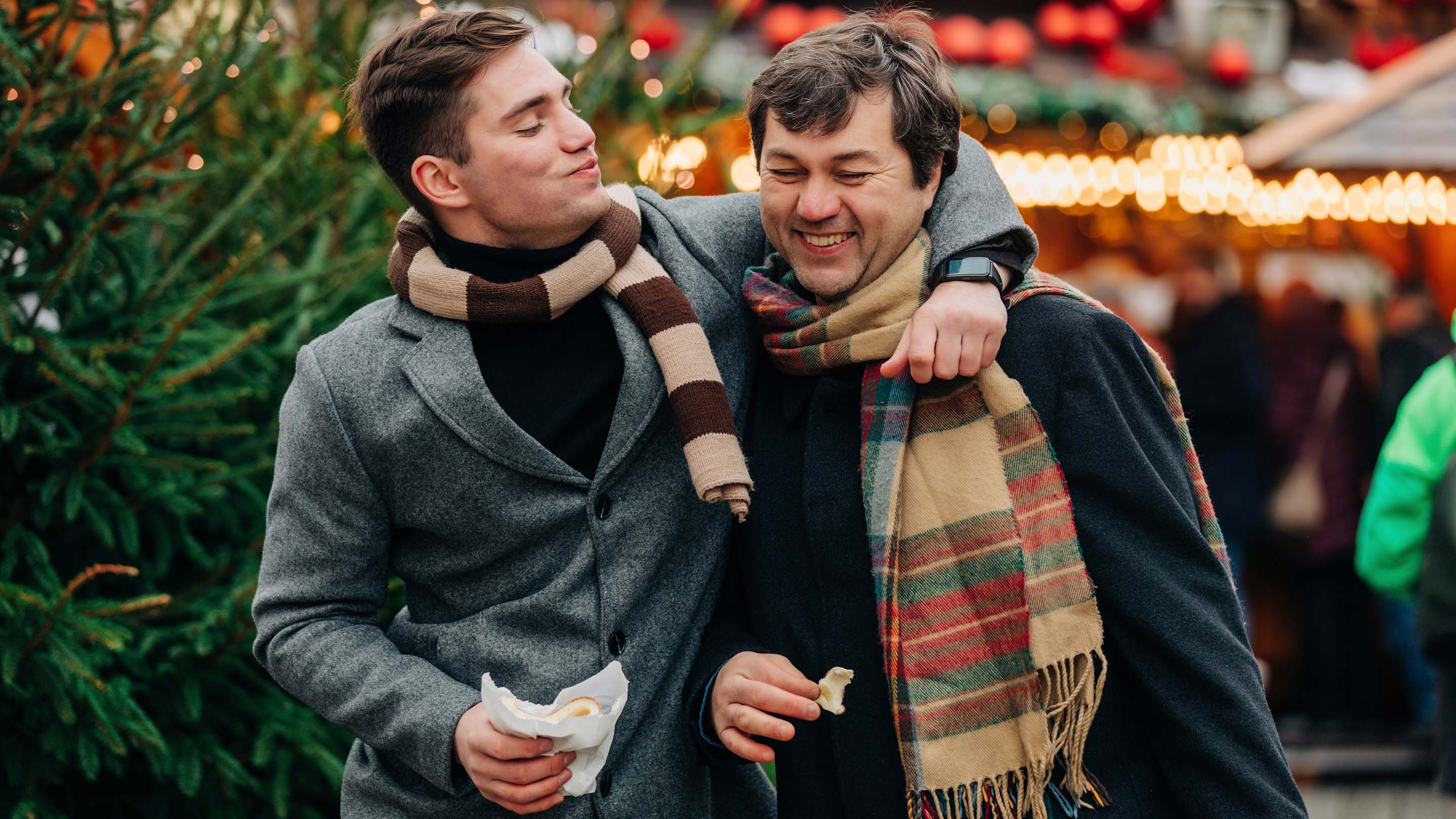 Smiling man with arm around father, enjoying themselves at Christmas market