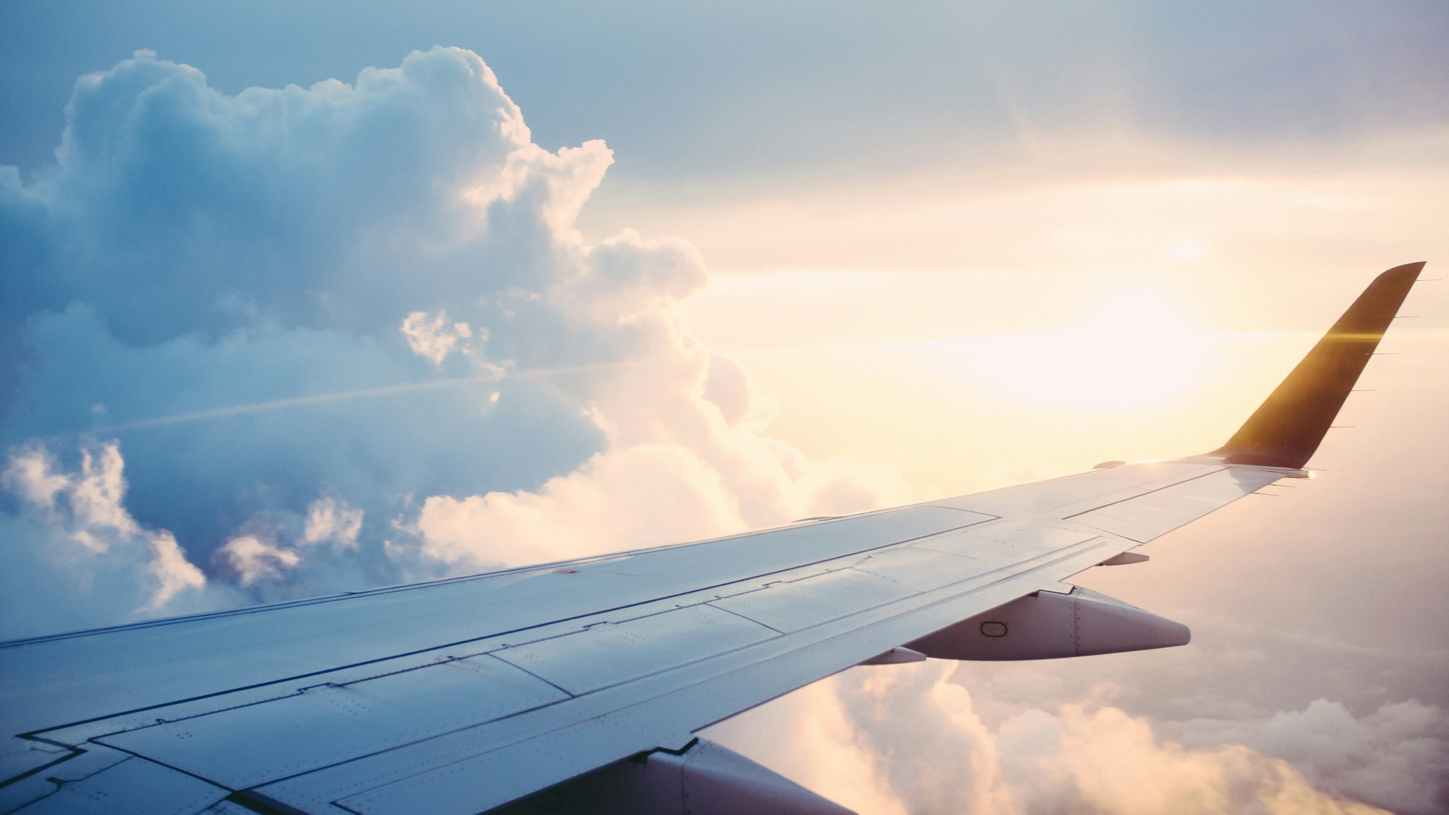 Aeroplane wing above soft clouds with sunlight breaking through the sky