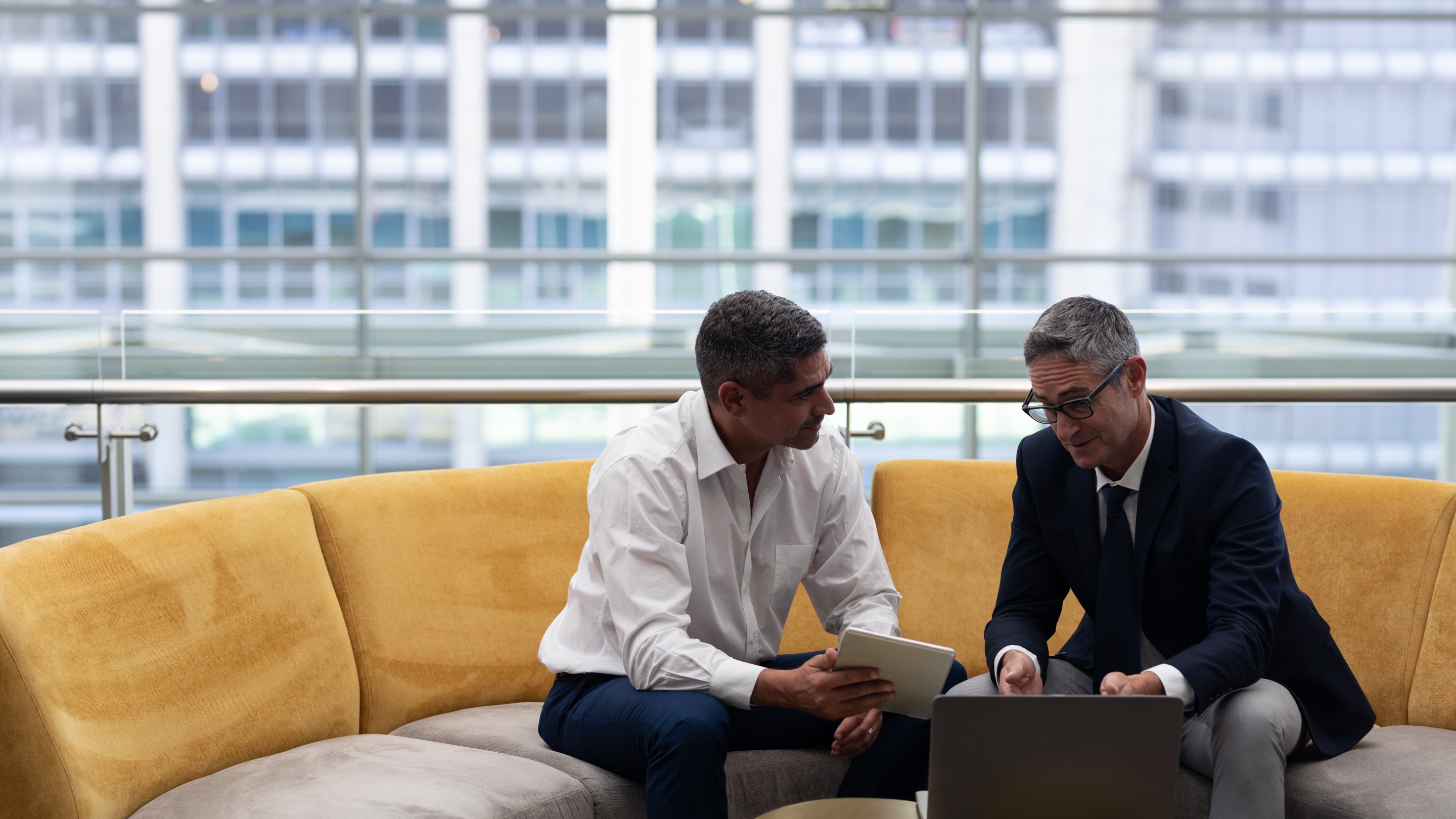 Two businessmen on sofa talking over laptop