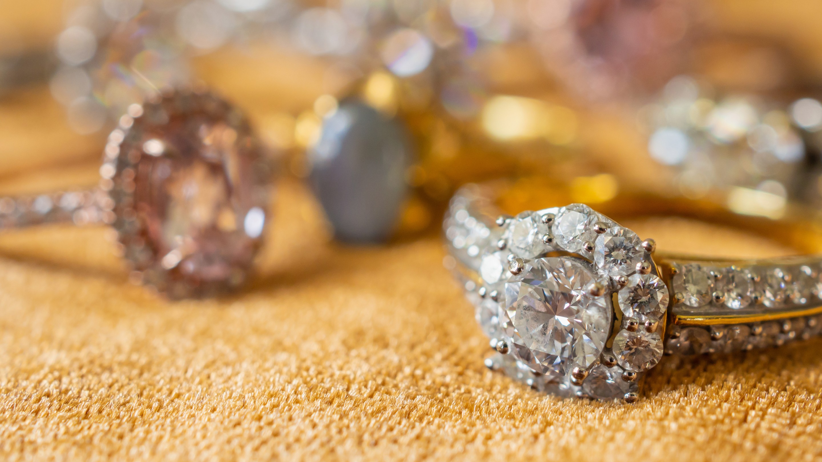 lose-up of diamond rings resting on a gold textured surface, with the nearest ring in sharp focus and others softly blurred in the background.