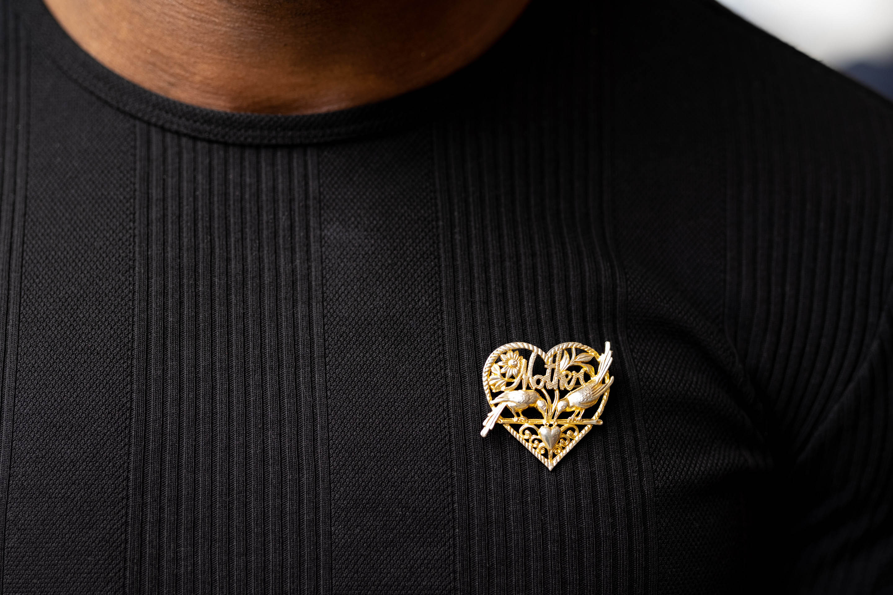 Kofi wearing his Nan's brooch. It's gold, heart shaped, features two birds and the word "Mother". It's pinned above his heart.
